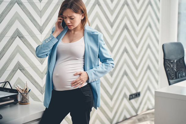 Upset pregnant woman talking on cellphone in office - 写真・画像