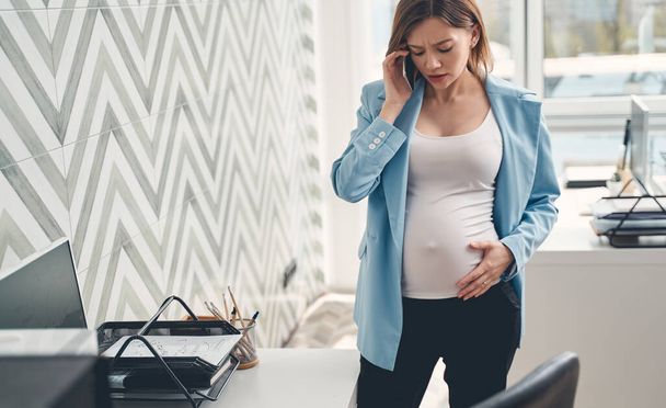 Disturbed pregnant lady talking on cellphone in office - Photo, image