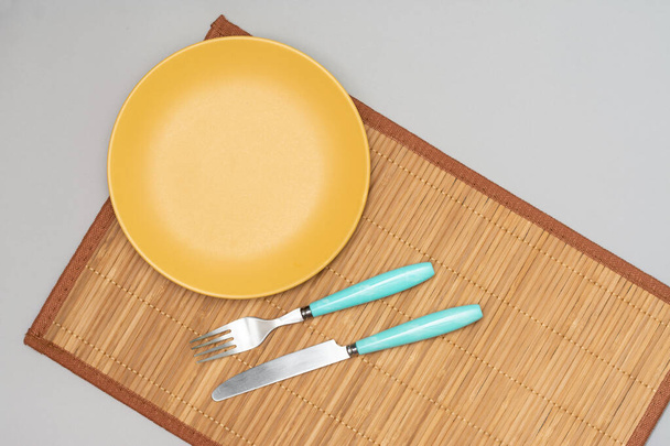 A yellow plate with a fork and knife on a Mat on a gray background. Top view with space for text - Foto, Imagem