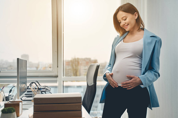 Joyful pregnant woman standing in modern office - Фото, изображение