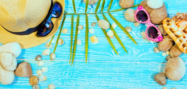 banner with beach accessories on a blue board aquamarine color background. Hat, sunglasses, sea shells, sea stones. Travel and tourism. Summer vacation concept. - Photo, Image