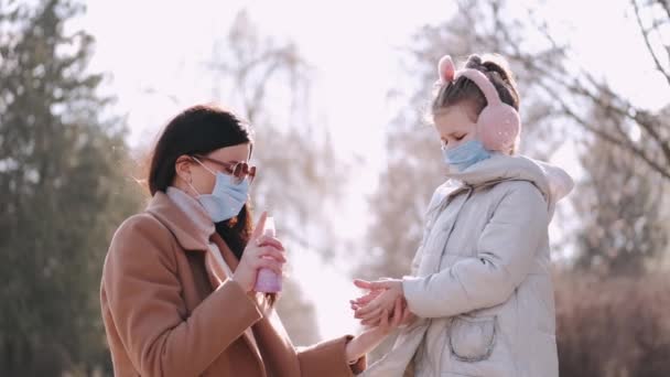 The mother is spraying antiseptical liquid on daughters handS in a park - Záběry, video