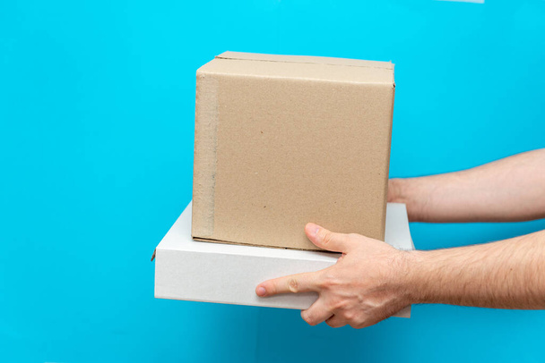 Ein Mann hält Schachteln in den Händen auf blauem Grund. Dienstleistungserbringung von Waren. Stadtlieferdienst. - Foto, Bild