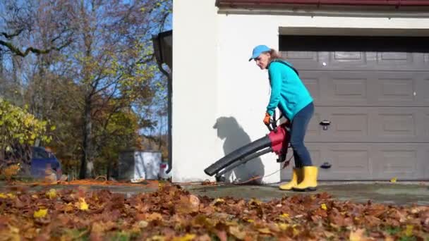 Hired girl blowing leaves from garage entrance in autumn - Footage, Video