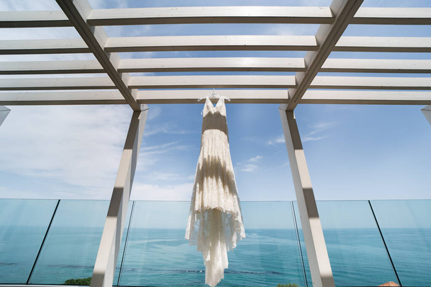Hochzeitskleid hängt an hölzernen Trennwänden. Blauer Sommerhimmel im Hintergrund. . - Foto, Bild