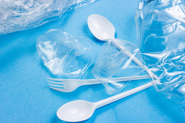Plastic lepels, vorken, flessen en bekers als wegwerpafval op een helderblauwe achtergrond. Milieuverontreiniging en recycling van zwerfvuil. - Foto, afbeelding