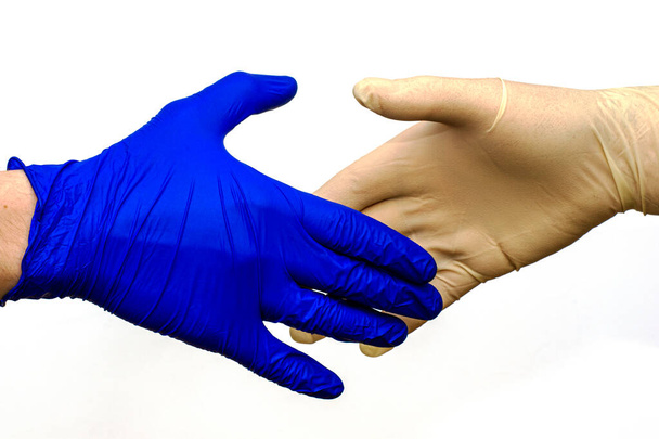 handshake of two hands in protective hygienic surgical gloves of different colors on a white background - Photo, Image
