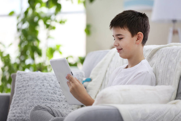 Niño pequeño usando la tableta en un sofá en casa
 - Foto, imagen