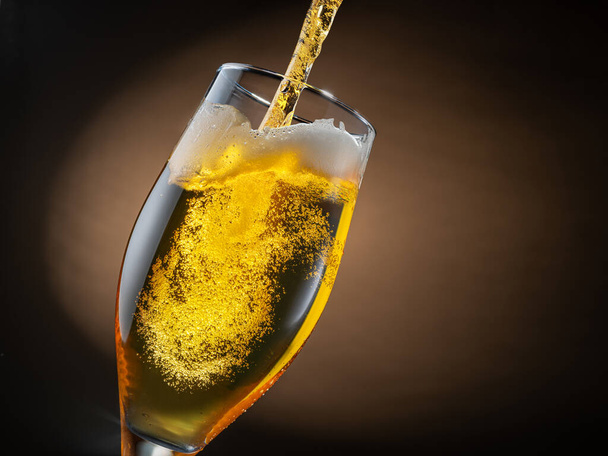 Jet of beer is poured into a beer glass, causing a lot of bubbles and foam. Dark brown background. - Valokuva, kuva
