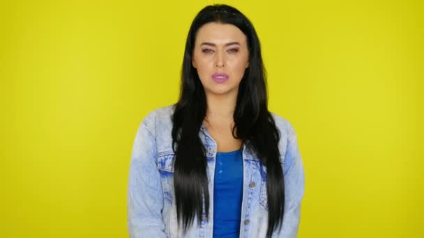 beledigde vrouw met zwart haar in spijkerjasje, gele achtergrond met copyspace - Video