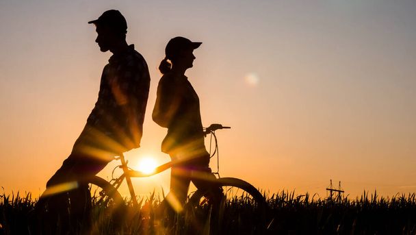 Un jeune couple admire le beau paysage au coucher du soleil, debout près du vélo
 - Photo, image