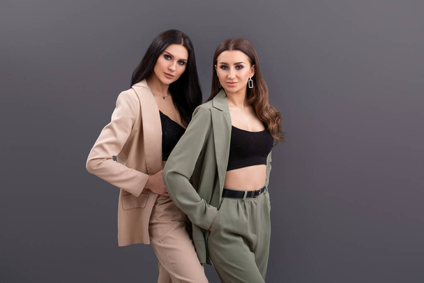 retrato de duas mulheres de negócios atraentes vestindo em ternos e tops posando em fundo cinza
 - Foto, Imagem