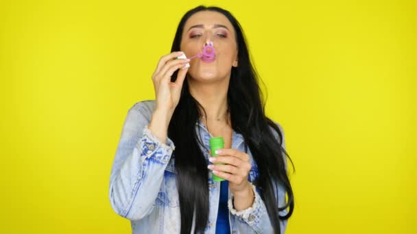 Woman inflates soap bubbles and smiles on a yellow background with copy space - Кадры, видео