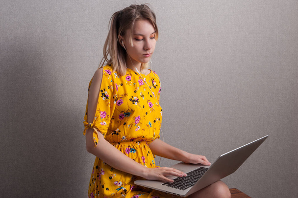 Nastolatka w żółtej sukience siedzi w domu i pracuje nad laptopem. Zostań w domu. - Zdjęcie, obraz