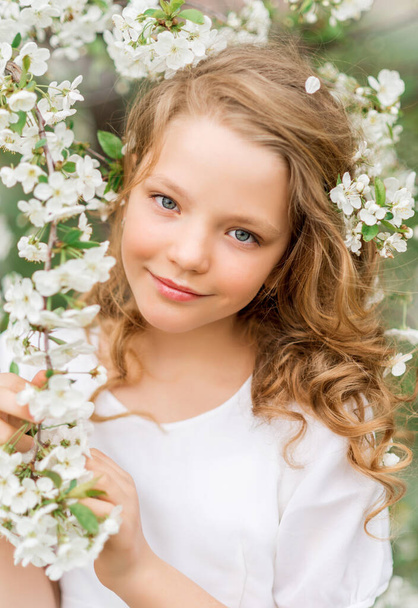 Portrait of a beautiful girl in a blooming garden in spring. Cute baby with white flowers in her hair. - Foto, afbeelding