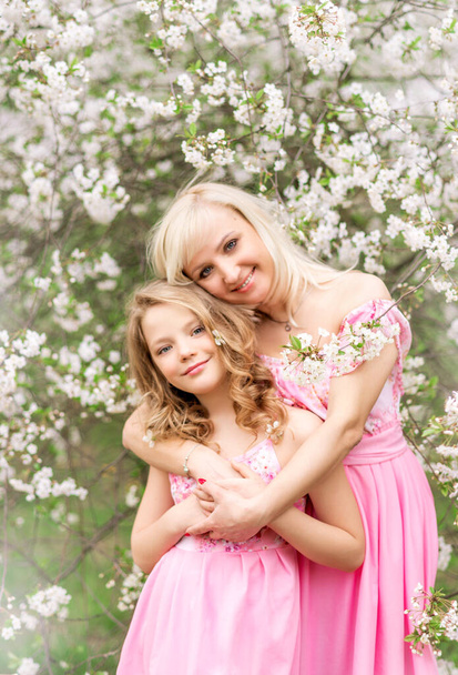 Мати і дочка в рожевих сукнях в квітучому саду навесні
. - Фото, зображення