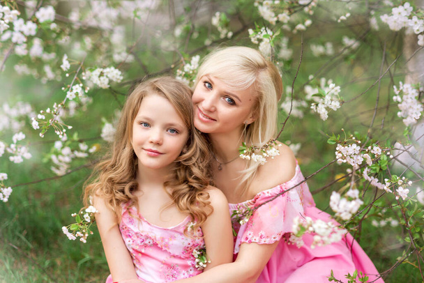 Anya és lánya rózsaszín ruhában egy virágzó kertben tavasszal. Egy közeli kép egy anyáról és lányáról.. - Fotó, kép