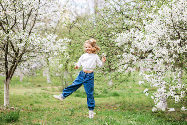 Bahar bahçesinde oynayan kot pantolonlu mutlu genç kız - Fotoğraf, Görsel