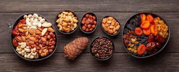 Various dried fruits and nuts on a dark wooden table. Top view flat lay - Photo, Image