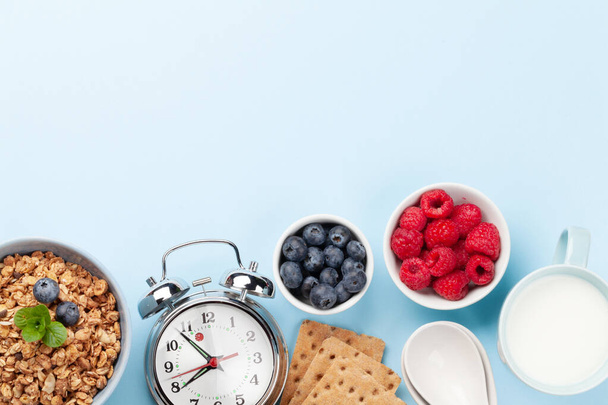 Zdrowe śniadanie z domowej roboty granolą z jogurtem i świeżymi jagodami na niebieskim tle. Poranny posiłek. Widok z góry z miejsca kopiowania - Zdjęcie, obraz