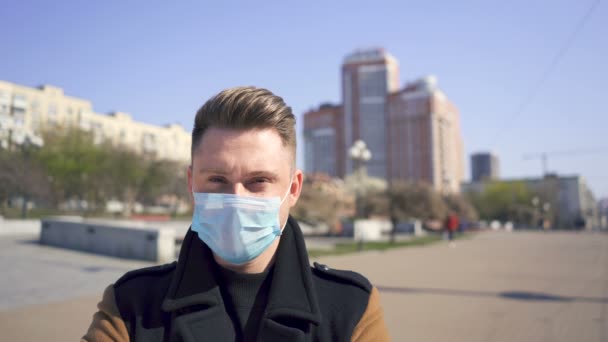 Blanke man zet een medisch masker op op lege straat. Close-up portret - Video