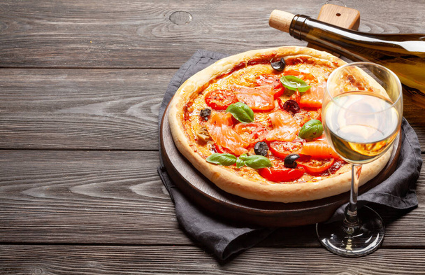 Smaczna pizza z owoców morza domowej roboty z pomidorami ogrodowymi, serem, łososiem i bazylią. Z białym winem i przestrzenią kopiującą - Zdjęcie, obraz