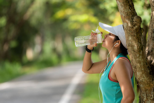 Gezonde atletische Aziatische vrouw is het drinken van puur water uit de fles verfrissend zichzelf na het sporten in het natuurpark. Gezond en lifestyle concept - Foto, afbeelding
