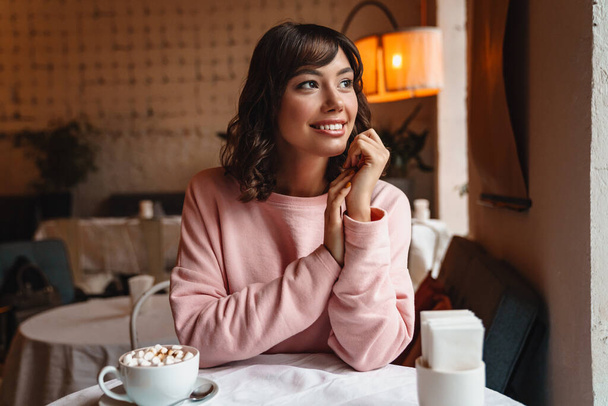 Image of a beautiful young cheerful optimistic happy woman indoors in cafe drinking coffee with marshmallow. - Foto, imagen