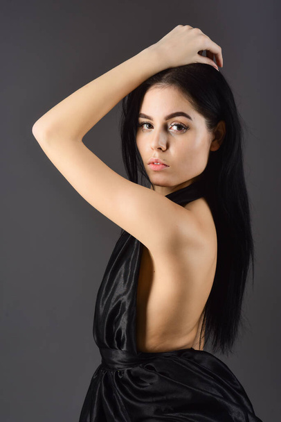 Lady, confident sexy girl in dress. Fashion concept. Attractive girl wears expensive fashionable evening dress with nude shoulders. Woman in elegant black dress with naked back, dark background. - Photo, Image