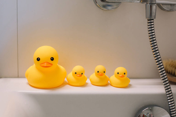 Acessórios de banho e quatro patos amarelos de borracha estão de pé no banheiro branco
 - Foto, Imagem
