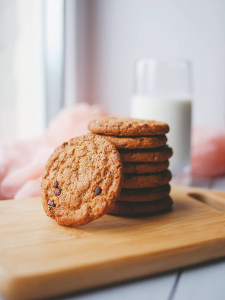 Tarçınlı ve bir bardak sütlü yulaf ezmeli çikolatalı kurabiye. Tahta kesme tahtasındaki kurabiyeler. - Fotoğraf, Görsel
