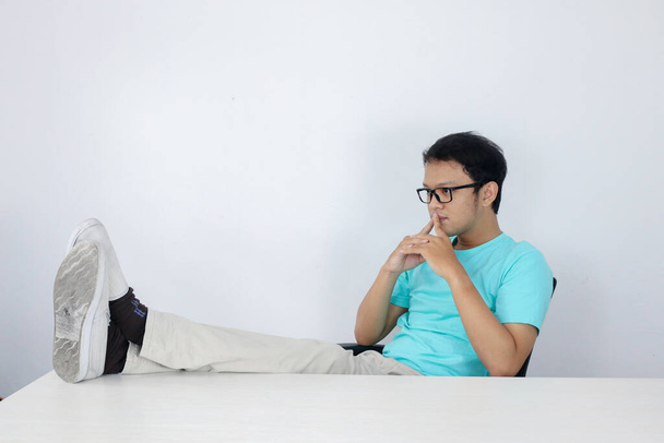 Young Asian Man with serious and focus look with leg on the table and arm on the chin. Indonesian man wearing blue shirt. - Fotó, kép