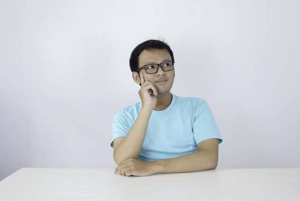 Young Asian man wear blue shirt and glasses with thinking and looking idea gesture in above empty space - Fotografie, Obrázek