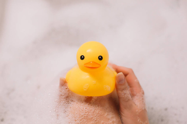 Fille tient canard en caoutchouc jaune dans le bain avec de la mousse à bulles
 - Photo, image