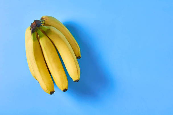 Ένα μάτσο φρέσκες ώριμες μπανάνες γεμάτες βιταμίνες σε μωβ φόντο. Χώρος για κείμενο. Άνω όψη - Φωτογραφία, εικόνα