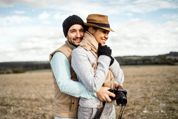 Νεαρό ζευγάρι με κάμερα αγκαλιάζει με αγάπη στη μέση του γηπέδου. - Φωτογραφία, εικόνα
