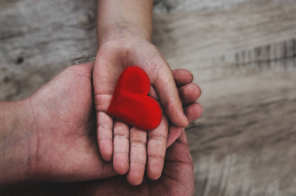 red heart in child and mother hands wooden background. concept of love, charity, empathy - Photo, Image