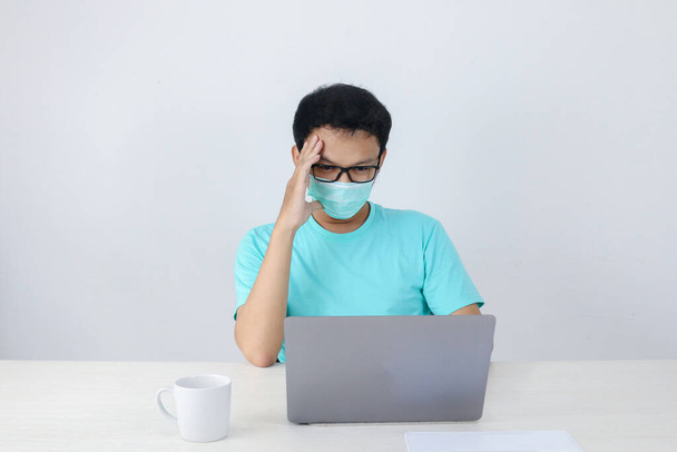 Young Asian man wearing medical mask is feeling unhealthy, tired, and confuse with work in laptop. - Foto, immagini
