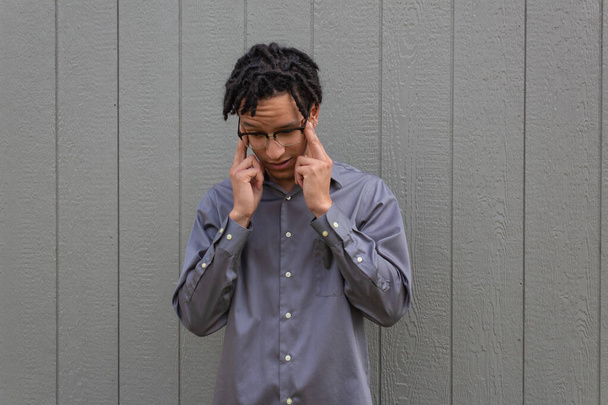 Junger Mann mit den Fingern zu den Schläfen, der nach unten schaut, Kopfschmerzen, birassischer Millennial-Afroamerikaner mit natürlichen Haaren in kurzen Dreadlocks, horizontaler Aspekt - Foto, Bild