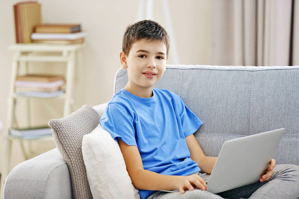 Boy with laptop sitting on a sofa at home - 写真・画像