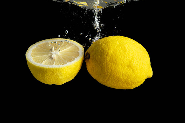 Fresh yellow lemon in water splash isolated on black background. Minimal food concept. - Photo, Image