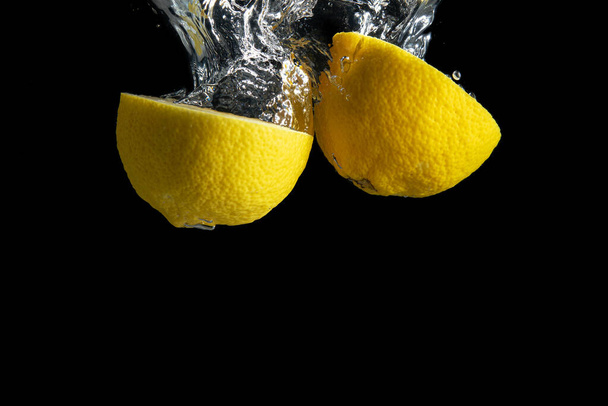 Fresh yellow lemon in water splash isolated on black background. Minimal food concept. - Photo, Image