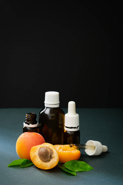 het concept van natuurlijke cosmetica, abrikozen met glazen flessen met olie op een donkere achtergrond - Foto, afbeelding
