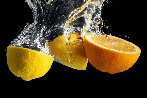 Fresh sliced orange and lemon in water splash isolated on black background. Minimal food concept. - Photo, Image