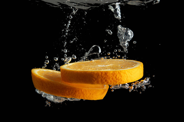 Свежие нарезанные апельсиновые фрукты в воде брызги изолированы на черном фоне. Минимальная концепция питания
. - Фото, изображение