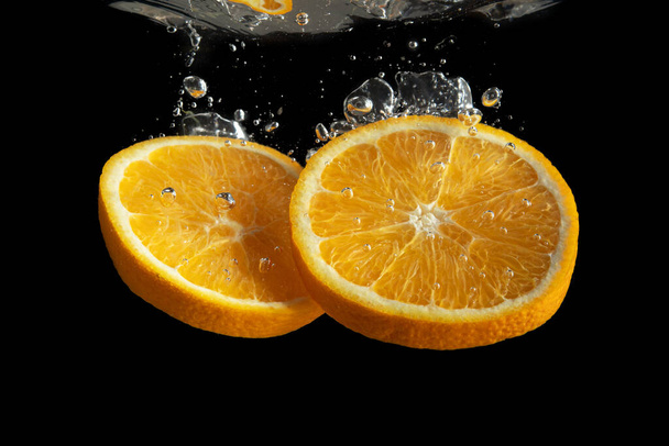 Fresh sliced orange fruit in water splash isolated on black background. Minimal food concept. - Foto, Bild