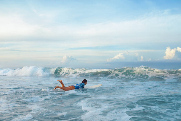 Surfen. Surfer Meisje Op Surfplank In Oceaan. Gelooide Brunette in blauw wetsuit zwemmen in spetterende zee. Watersport voor een actieve levensstijl. - Foto, afbeelding
