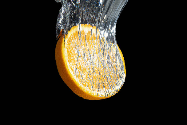 Fresh sliced orange fruit in water splash isolated on black background. Minimal food concept. - Photo, Image
