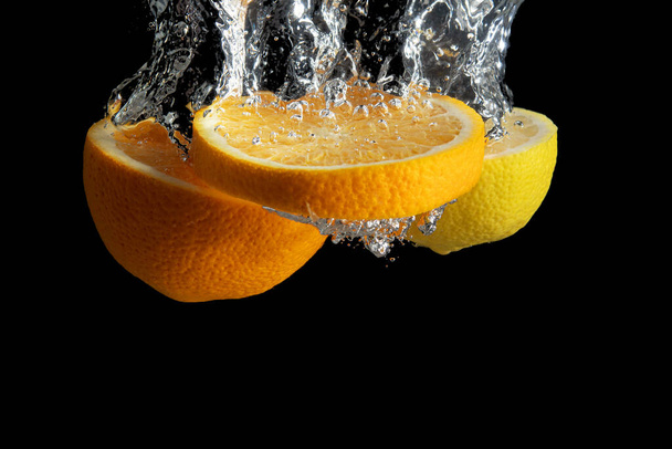 Frisch geschnittene Orangen und Zitronen in Wasser spritzen isoliert auf schwarzem Hintergrund. Minimales Ernährungskonzept. - Foto, Bild