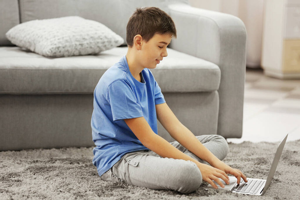 Menino usando laptop em um tapete em casa
 - Foto, Imagem